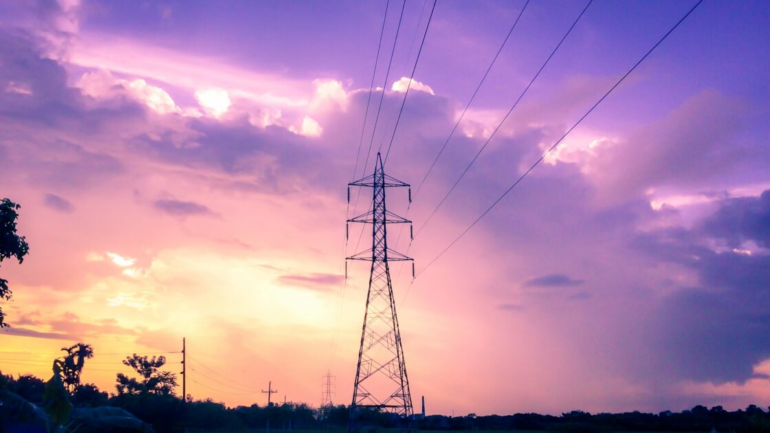 High-voltage transmission tower and power lines against sunset sky representing grid infrastructure expansion