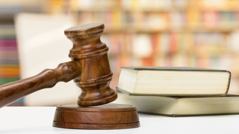 A judge’s gavel resting beside two closed legal books with a blurred bookshelf in the background.