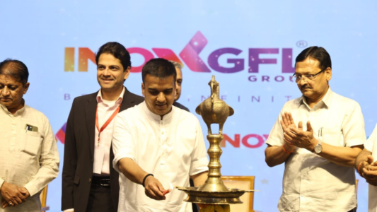 Gujarat Deputy Chief Minister lighting a ceremonial lamp during the inauguration of INOXGFL Group’s solar and wind manufacturing facilities near Ahmedabad, with company and government officials on stage.