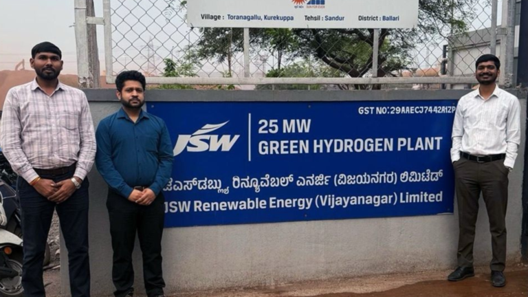 Employees standing beside a signboard reading “25 MW Green Hydrogen Plant – JSW Renewable Energy (Vijayanagar) Limited” at the Vijayanagar steel complex in Ballari, Karnataka