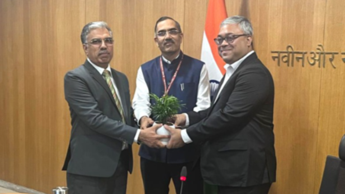 ACME Group representatives and SECI officials exchange a plant during the signing of a green ammonia supply agreement in a conference room, with the Indian flag visible in the background