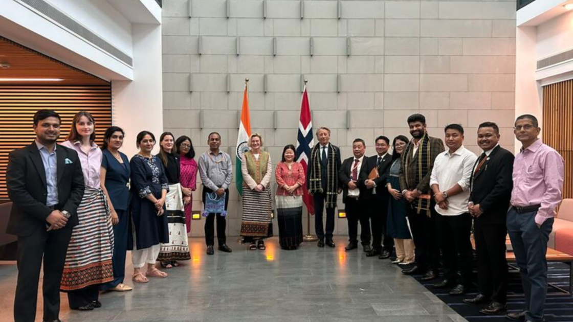 Group photograph of Indian and Norwegian delegates standing in a conference hall beside the national flags of India and Norway during an official meeting on renewable energy collaboration.